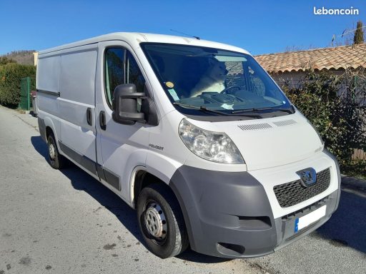 Fourgon utilitaire blanc garé sur une route, avec des paysages environnants.
